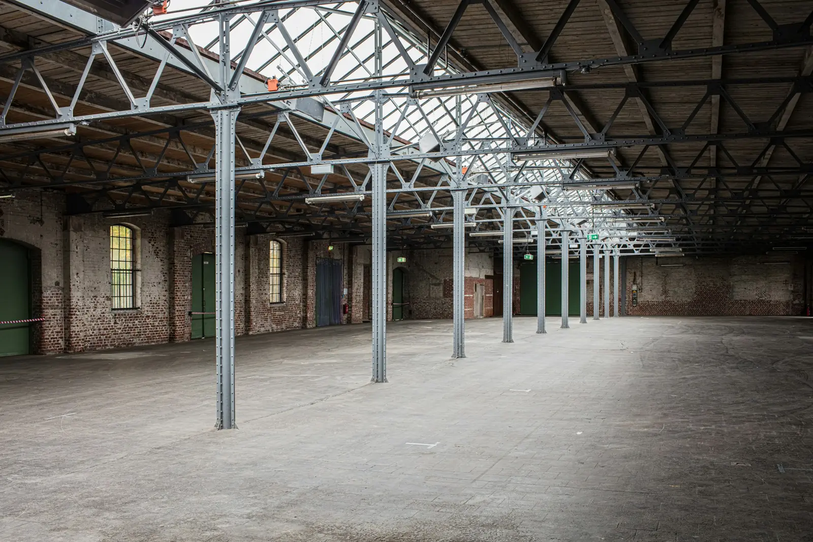 Alte, leere Industriehalle mit Stahlfachwerk, Oberlichtern und Backsteinwänden, Symbolbild